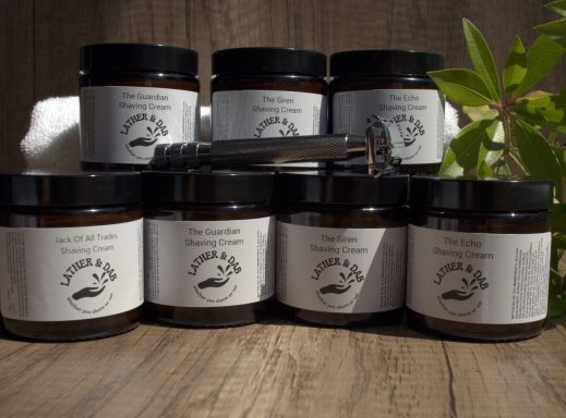 Group image of jars of handmade shaving cream, with a white towel in the background and a little foliage to the right. 