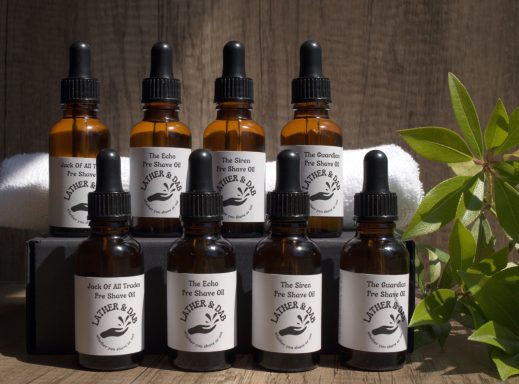 Group image of bottles of handmade Pre Shave oils. with a white towel in the background and a little foliage to the right. 