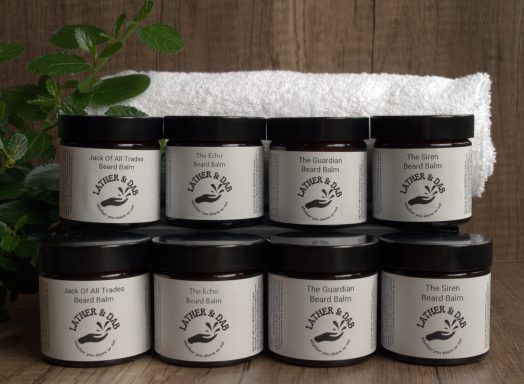 Group image of handmade beard balms,  with a white towel in the background and a little foliage to the right. 