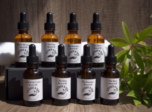 Group image of bottles of handmade Beard oils , with a white towel in the background and a little foliage to the right. 